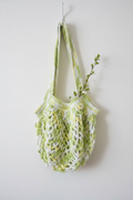 Green and white variegated crochet market bag hanging on a clean white wall