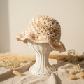 Handmade crochet bucket hat in cream and tan variegated yarn on wicker stand with pampas grass